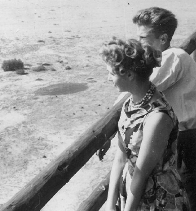 Fotografia czarno-biała. Młoda para, dziewczyna i chłopak stoją, opierając się o drewniane bele. Przed nimi rozciąga się widok na Pustynię Błędowską