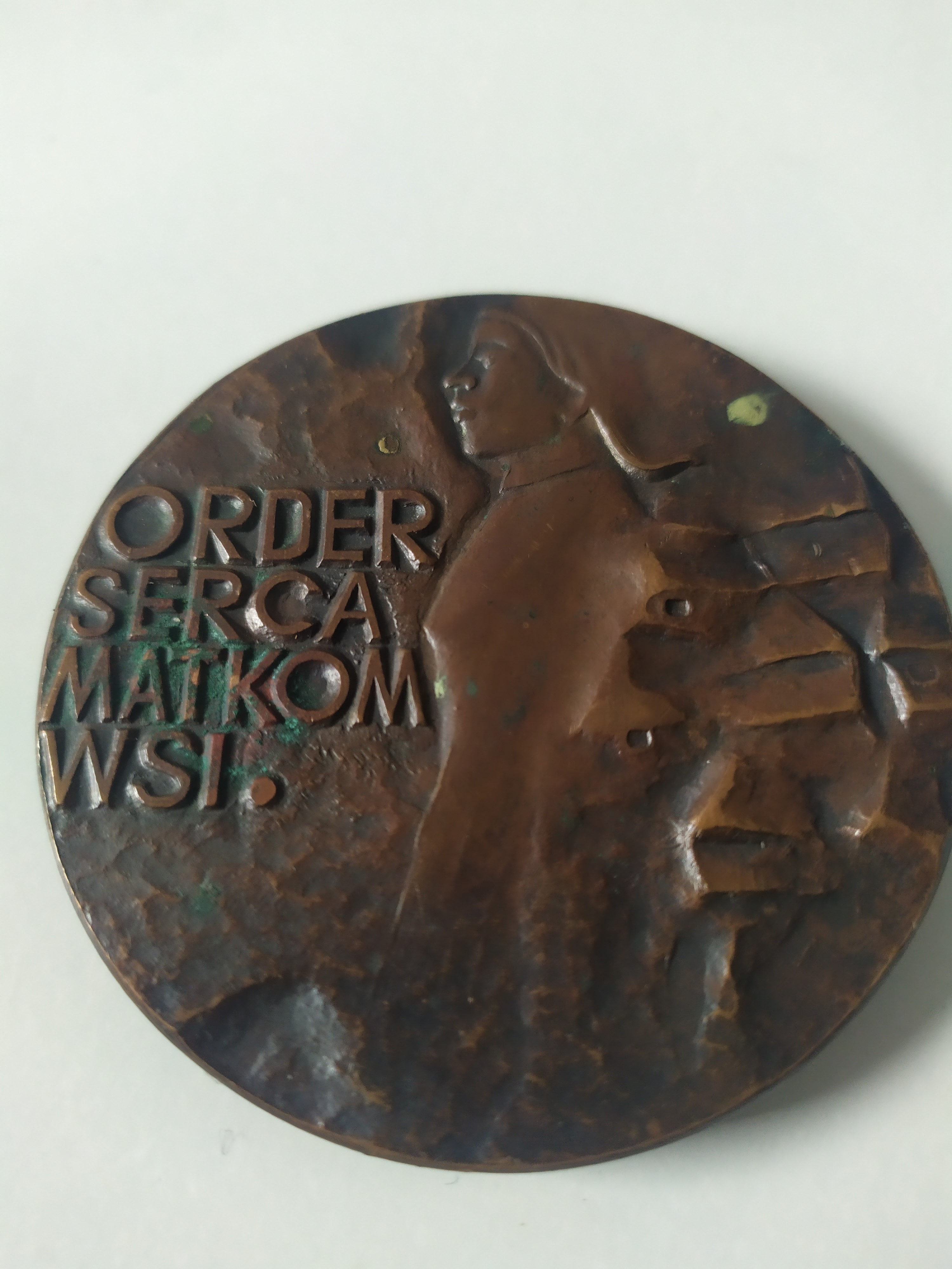 Okrągły medal z brązu z wypukłym profilem postaci i wygrawerowanym napisem „ORDER SERCA MATKOM WSI”.