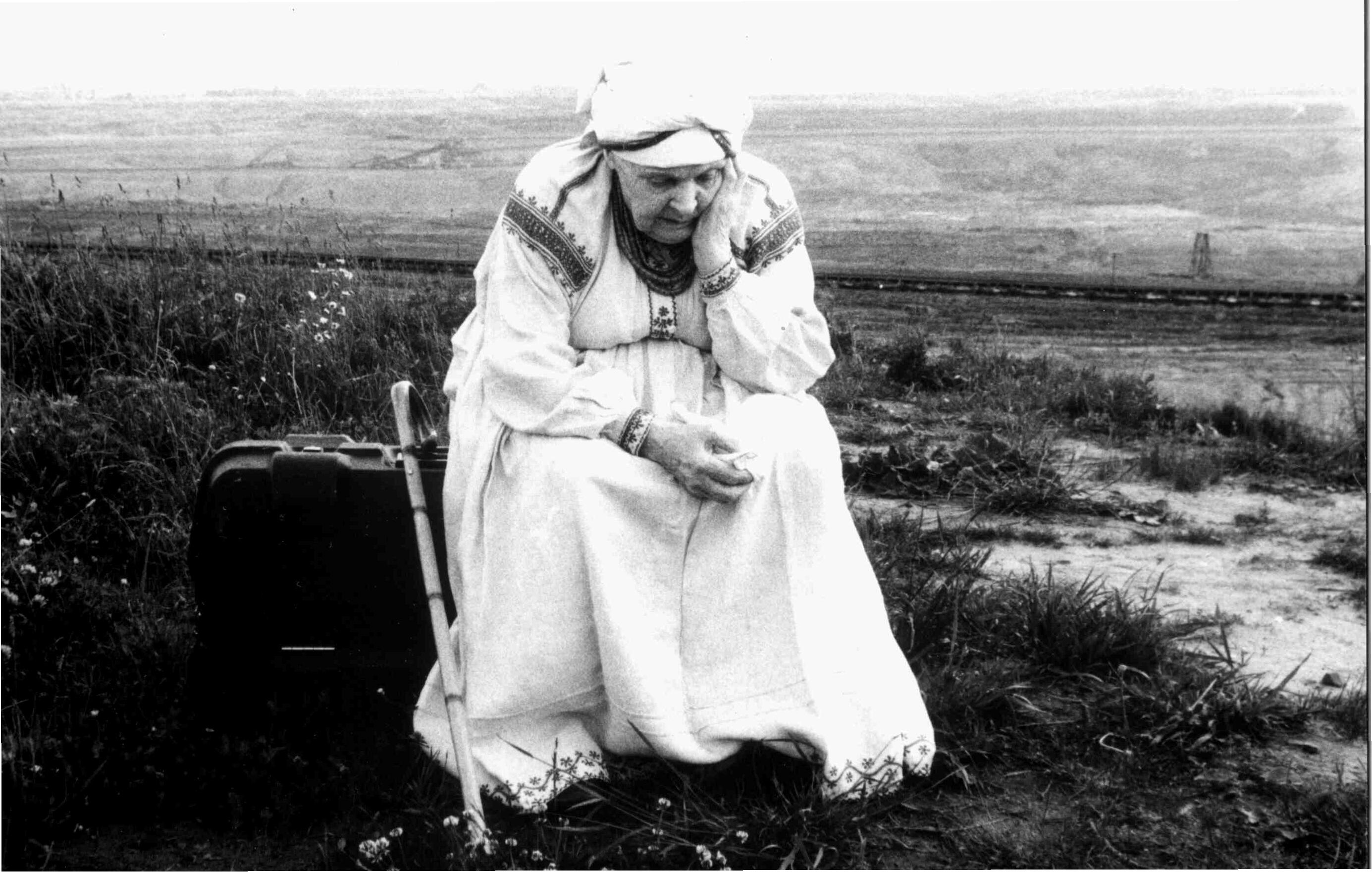 An old woman sits on the ground with a suitcase.