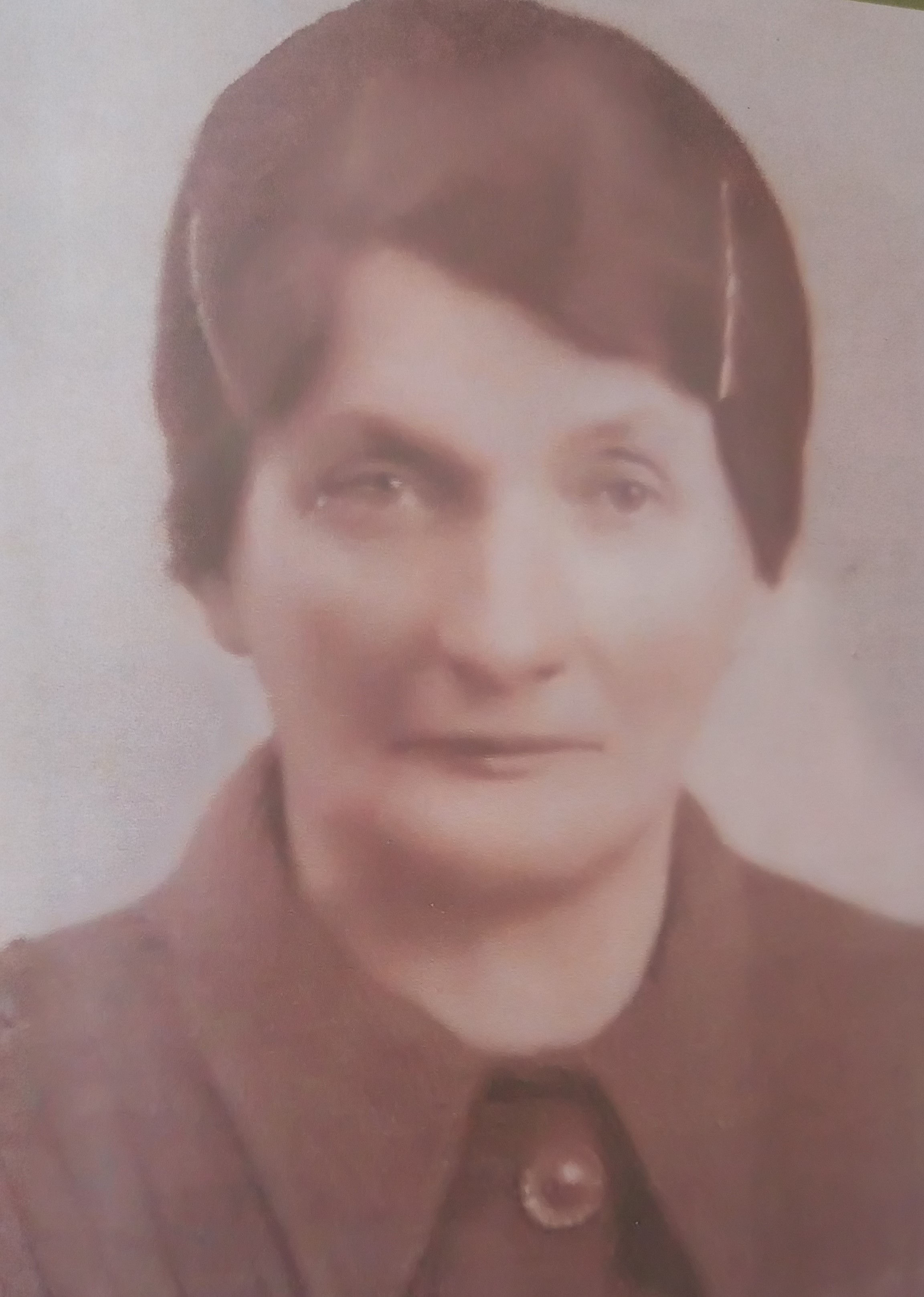 Portret w odcieniach sepii przedstawiający starszą osobę o krótkich, ciemnych włosach, ubraną w płaszcz z kołnierzykiem i guzikiem.