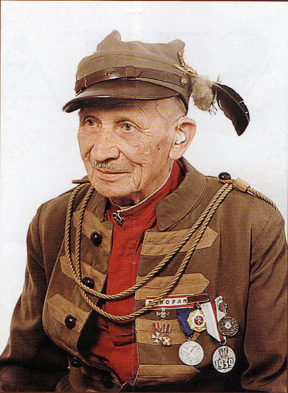 Starszy mężczyzna w zabytkowym mundurze wojskowym z czapką z piórami, z medalami i sznurami.