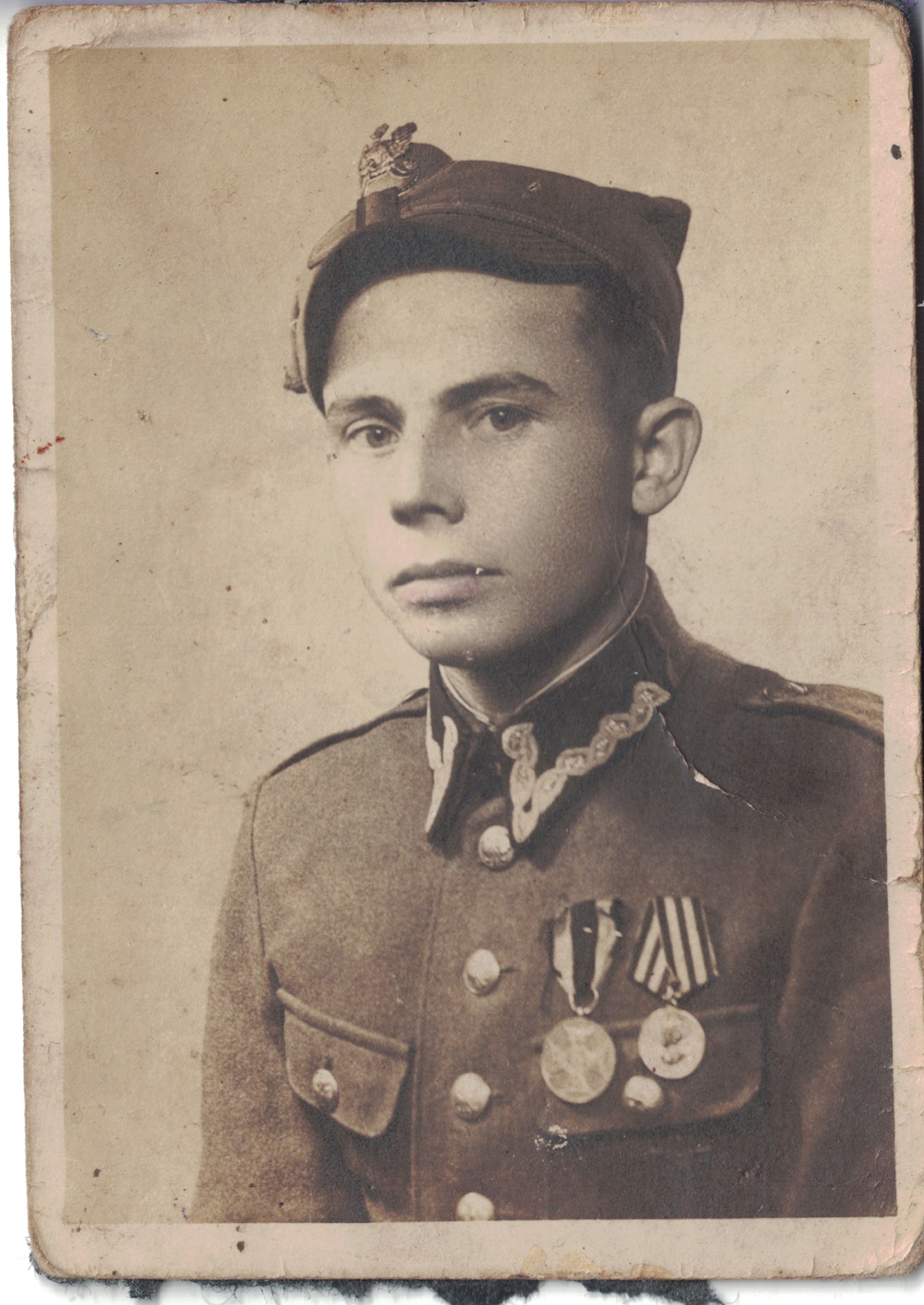 Czarno-białe zdjęcie młodego żołnierza w mundurze, z medalami i czapką z emblematem.