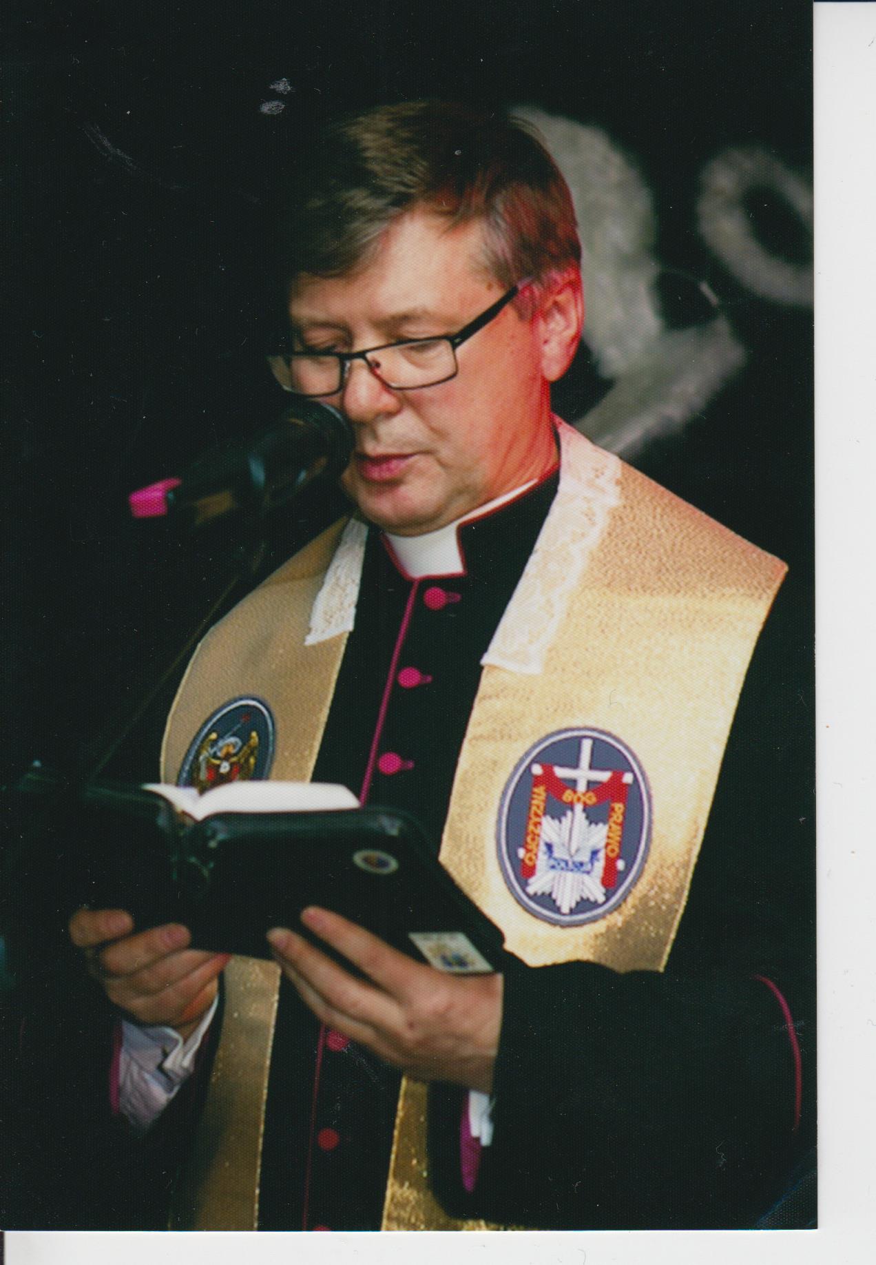 Ksiądz czyta książkę przed mikrofonem.
