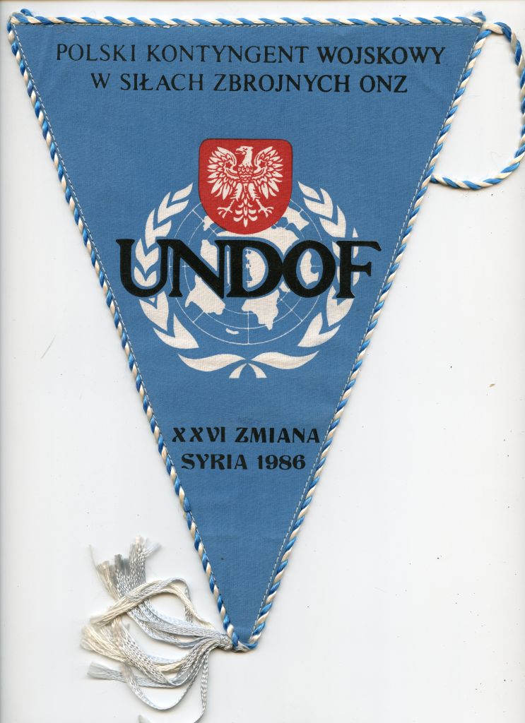 Niebieski proporczyk z polskim godłem wojskowym, insygniami UNDOF i napisem: „POLSKI KONTYNGENT WOJSKOWY W SIŁACH ZBROJNYCH ONZ XXVI ZMIANA SYRIA 1986.