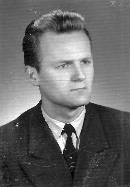 Czarno-biały portret mężczyzny w garniturze i krawacie, patrzącego w bok na jednolitym tle.