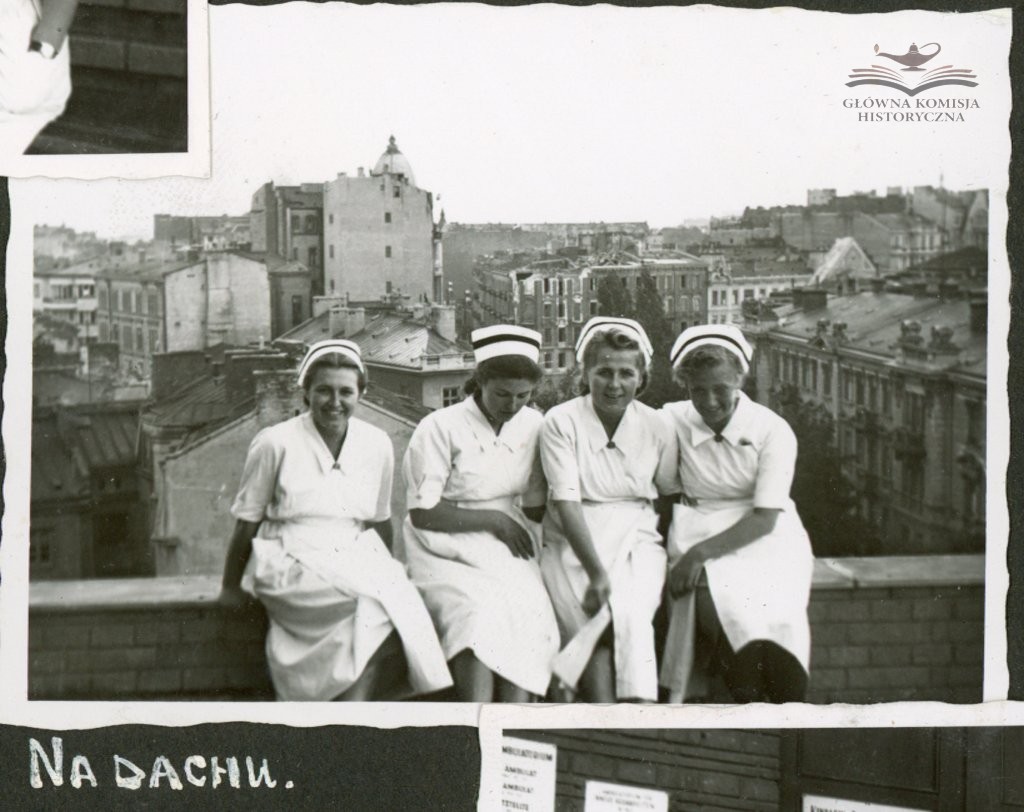 Four nurses in uniform sit on the cornice of the roof with the city skyline in the background; The Polish text and logo of the historical commission are visible.