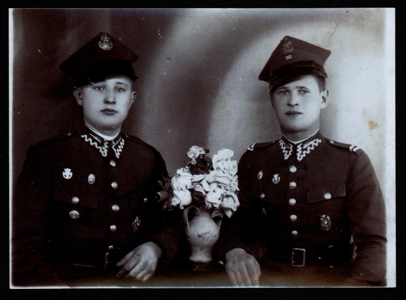 Dwóch mężczyzn w mundurach stojących obok wazonu.