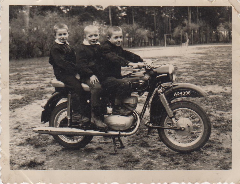 Czarno-białe zdjęcie trzech chłopców na motocyklu.