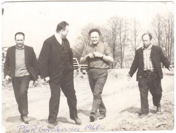 Czterech mężczyzn idących po ścieżce gruntowej w 1968 r., na tle nagich drzew. Na dole ręcznie napisany podpis: „PGR Grodziec 1968”.
