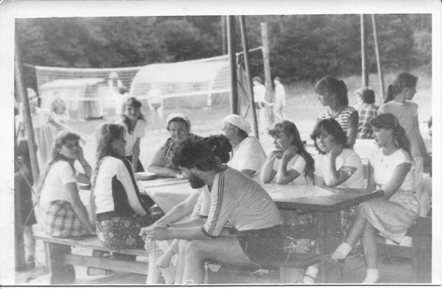 Grupa ludzi siedzących przy stole piknikowym.